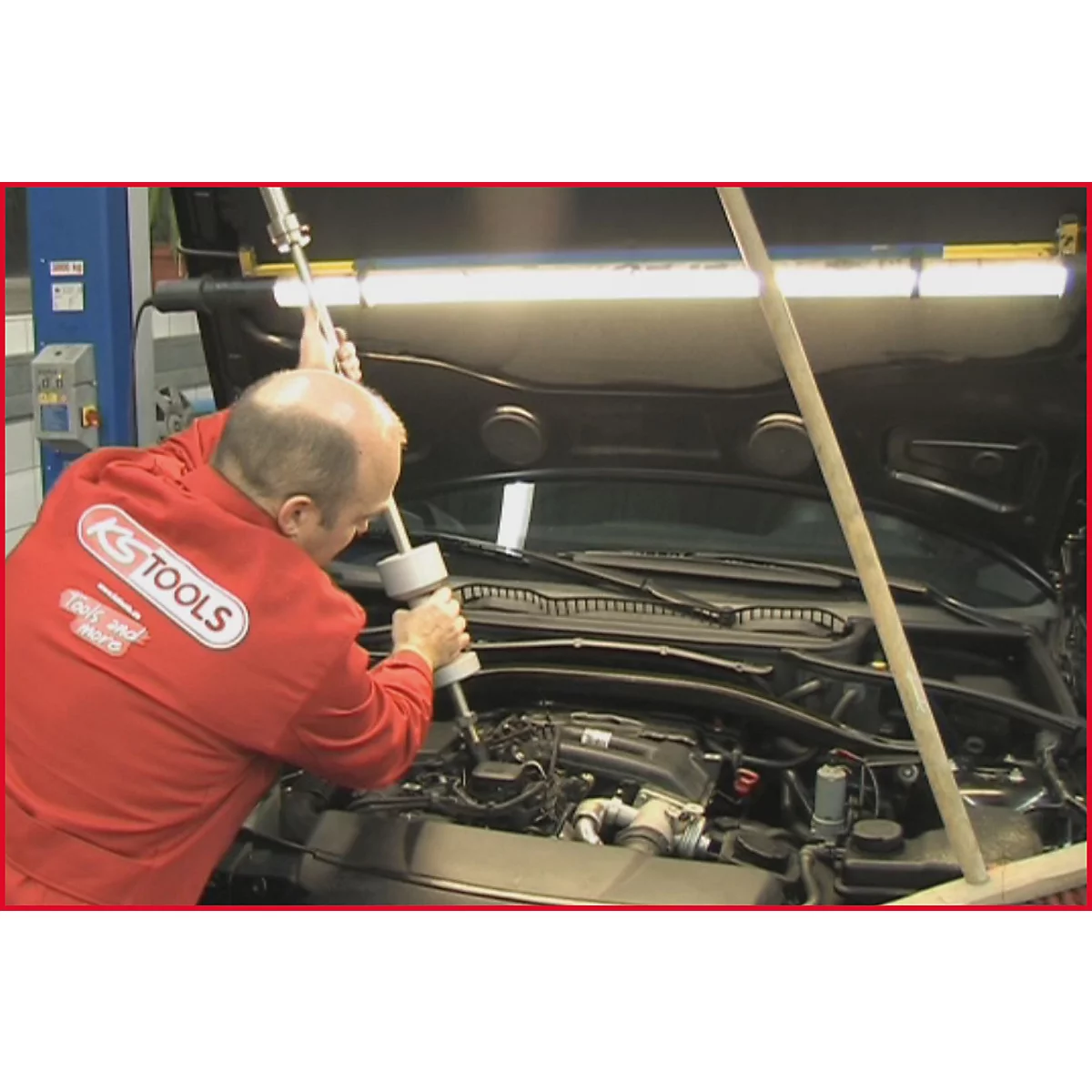 Mechaniker in rotem Overall von KS TOOLS arbeitet an einem Motorraum. Werkzeug im Einsatz.